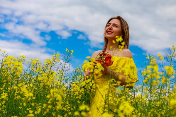 菜の花畑の明るい黄色の背景の雷の上に黄色のドレスの若いかなりの女性 自然との一体性の概念 — ストック写真