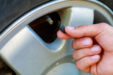 El, arabanın tekerleğindeki meme ucu kapağını büker ya da açar. Havalandırma lastiklerini yerleştirin. Metin veya harf için kopyalama alanı olan tonlanmış arkaplan. Şapkaya odaklan..