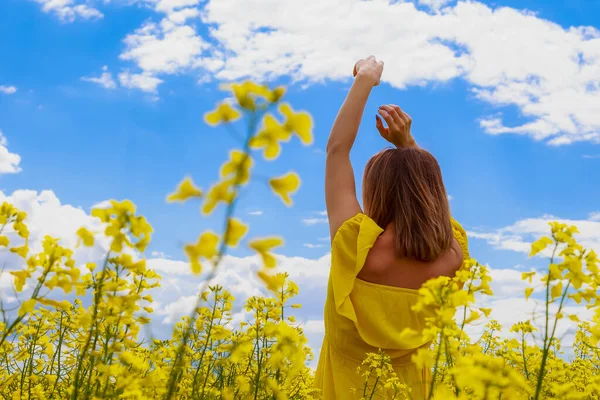 菜の花畑の明るい黄色の背景の雷の上に黄色のドレスの若いかなりの女性 喜びの概念 — ストック写真