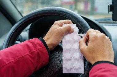 Sürücü, arabadaki direksiyonun bulanık arka planına karşı bir hap paketi açar. Araba kullanırken tıbbi amaçlar için farmakolojik ilaç kullanımı. Seçici odaklanma, tonlama