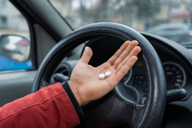 Two pills in the hand or on the palm of the driver against a blurred background of the steering wheel in the car. The use of pharmacological drugs for medical purposes while driving. Selective focus clipart
