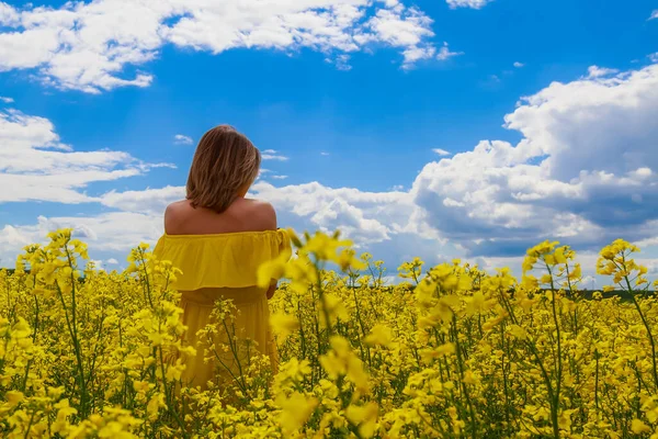 菜の花畑の明るい黄色の背景の雷の上に黄色のドレスの若いかなりの女性 喜びの概念 — ストック写真