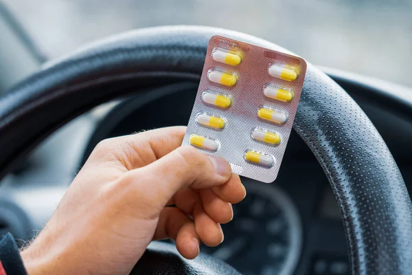 Blister of pills in the hands of the driver on a blurred background of the steering wheel in the car. The use of pharmacological drugs for medical purposes while driving. Selective focus