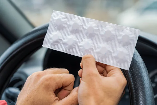 stock image Pack of pills in the hands of the driver on a blurred background of the steering wheel in the car. The use of pharmacological drugs for medical purposes while driving. Selective focus