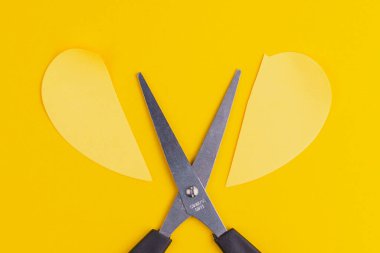 Makas kağıt kalbi ikiye böldü. İlişki kırma konsepti. Metin için kopyalama alanı olan sarı arkaplan