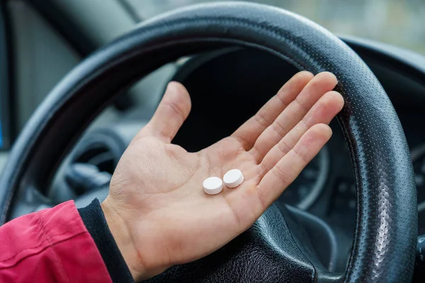 Two pills in the hand or on the palm of the driver against a blurred background of the steering wheel in the car. The use of pharmacological drugs for medical purposes while driving. Selective focus