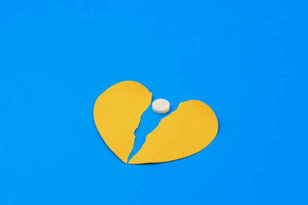 A classic medical white pill with a score and a heart shaped sticker torn in half. Selective focus on the pill. Background with copy space for text.