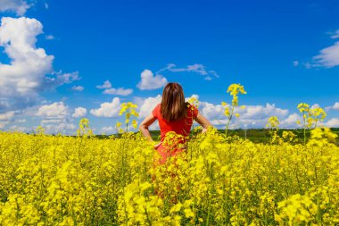 Renkli elbiseli, parlak sarı arka planda, çiçek açan kolza tohumu tarlasında genç, güzel bir kadın. Özgürlük kavramı