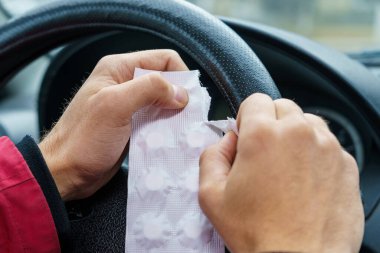 Sürücü, arabadaki direksiyonun bulanık arka planına karşı bir hap paketi açar. Araba kullanırken tıbbi amaçlar için farmakolojik ilaç kullanımı. Seçici odaklanma, tonlama