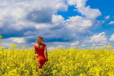 Renkli elbiseli, parlak sarı arka planda, çiçek açan kolza tohumu tarlasında genç, güzel bir kadın. Özgürlük kavramı