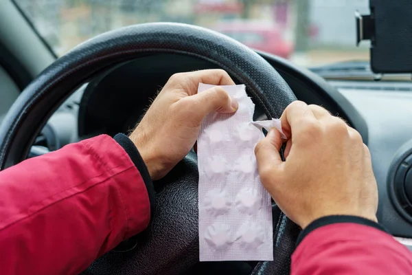 Sürücü, arabadaki direksiyonun bulanık arka planına karşı bir hap paketi açar. Araba kullanırken tıbbi amaçlar için farmakolojik ilaç kullanımı. Seçici odaklanma, tonlama