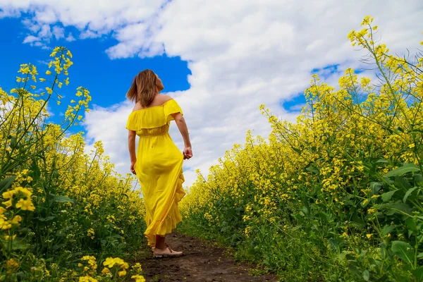 菜の花畑の明るい黄色の背景の雷の上に黄色のドレスの若いかなりの女性 喜びの概念 — ストック写真