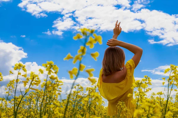 菜の花畑の明るい黄色の背景の雷の上に黄色のドレスの若いかなりの女性 幸福の概念 — ストック写真