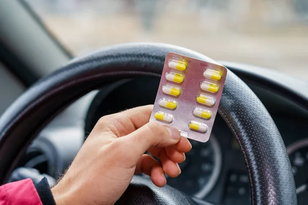 Blister of pills in the hands of the driver on a blurred background of the steering wheel in the car. The use of pharmacological drugs for medical purposes while driving. Selective focus