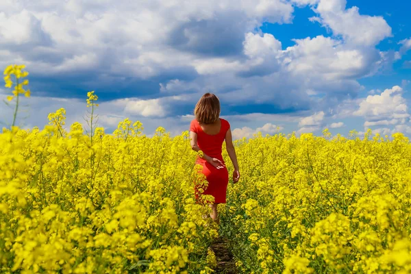 菜の花畑の明るい黄色の背景に雷の色のドレスで若いきれいな女性 幸福の概念 — ストック写真