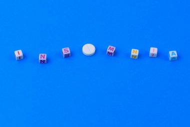 İnsomNIA metni küpten yapılmış. O harfi yerine puanı olan beyaz bir ilaç. Klasik geleneksel mavi arkaplan.