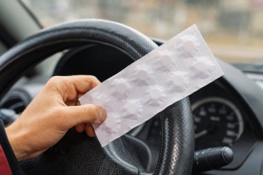 Pack of pills in the hands of the driver on a blurred background of the steering wheel in the car. The use of pharmacological drugs for medical purposes while driving. Selective focus clipart