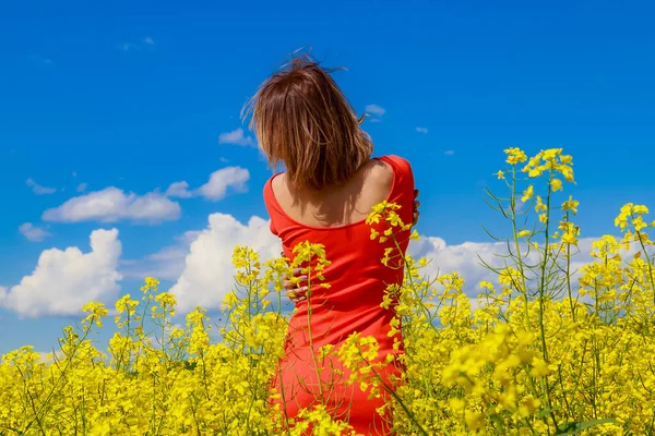 菜の花畑の明るい黄色の背景に雷の色のドレスで若いきれいな女性 喜びの概念 — ストック写真