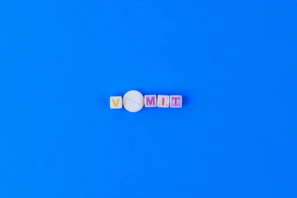文字Oの代わりにスコアを持つ白い医療用錠剤 キューブで作られたVomitテキスト 古典的な青の背景 — ストック写真