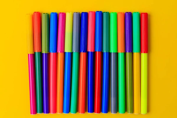 Multi-colored markers with mixed caps. Creative concept. Yellow background with selective focus and copy space for text