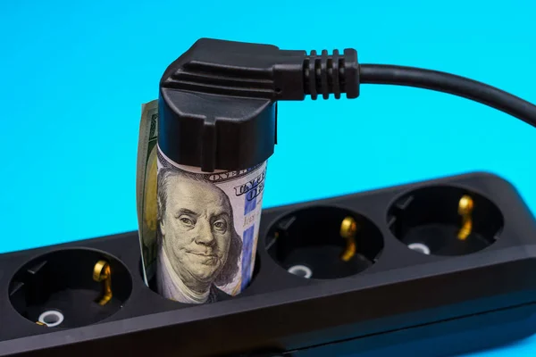 Rolled dollar bills in power strip sockets. The concept of the energy crisis and electricity inflation. Rising electricity prices. Copy space for text.