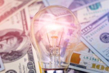 Dolar banknotları ya da banknotların bulanık arka planında klasik elektrik ampulü. Enerji krizi ve elektrik enflasyonu kavramı. Elektrik fiyatlarında artış. Metin için alanı kopyala.