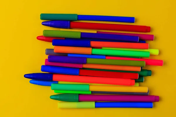 Multi-colored markers with mixed caps. Creative concept. Yellow background with selective focus and copy space for text