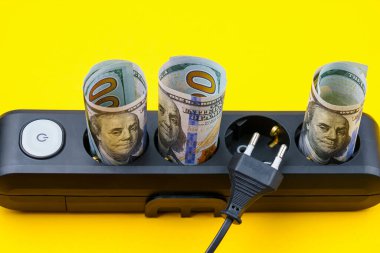 Elektrik prizlerinde yuvarlanmış dolar banknotları. Enerji krizi ve elektrik enflasyonu kavramı. Artan elektrik fiyatları. Metin için alanı kopyala.
