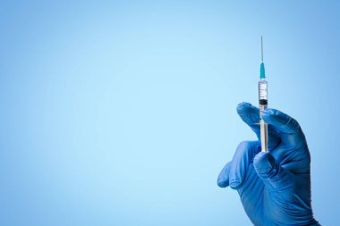 Doctors hand in surgical gloves holds a syringe on a classic symbolic blue background