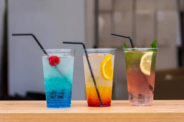 Close up of three fruit cooling refreshing cocktails in transparent disposable glasses with straws for sale at the international street food festival, selective focus. Background with copy space