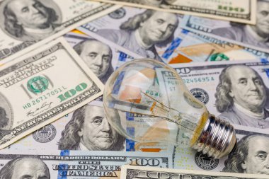 Dolar banknotları ya da banknotların bulanık arka planında klasik elektrik ampulü. Enerji krizi ve elektrik enflasyonu kavramı. Elektrik fiyatlarında artış. Metin için alanı kopyala.