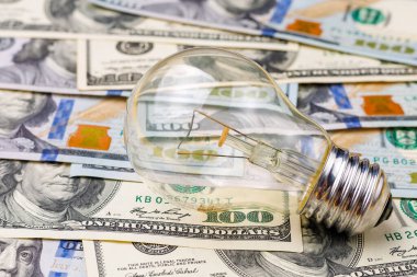 Dolar banknotları ya da banknotların bulanık arka planında klasik elektrik ampulü. Enerji krizi ve elektrik enflasyonu kavramı. Elektrik fiyatlarında artış. Metin için alanı kopyala.
