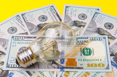 Dolar banknotları ya da banknotların bulanık arka planında klasik elektrik ampulü. Enerji krizi ve elektrik enflasyonu kavramı. Elektrik fiyatlarında artış. Metin için alanı kopyala.