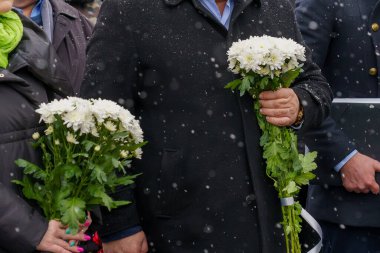 Flowers in hands at a solemn laying ceremony or a memorial day of mourning in bad winter weather under snow. Background with selective focus and copy space for text