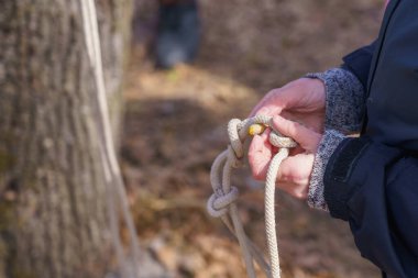 Bir turistin elleri, seçici bir odak noktasıyla ipte düğüm atıyor. Metin için kopyalama alanı olan arkaplan