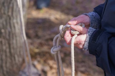 Bir turistin elleri, seçici bir odak noktasıyla ipte düğüm atıyor. Metin için kopyalama alanı olan arkaplan
