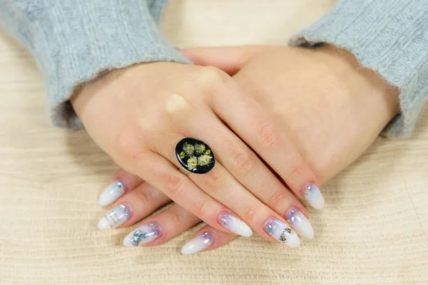 Transparent ring with flowers on the ring finger of the right female hand. Homemade epoxy resin jewelry. Rare interesting unusual hobby. Background with selective focus and copy space for text