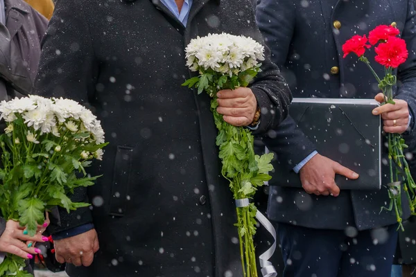 Flowers in hands at a solemn laying ceremony or a memorial day of mourning in bad winter weather under snow. Background with selective focus and copy space for text