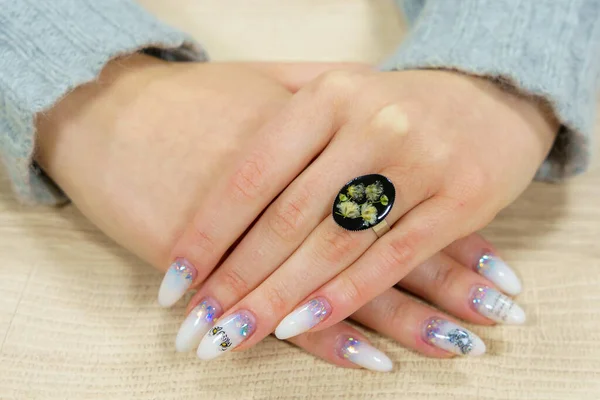 Transparent ring with flowers on the ring finger of the left female hand. Homemade epoxy resin jewelry. Rare interesting unusual hobby. Background with selective focus and copy space for text
