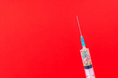 Sembolik kalplerle dolu tek kullanımlık klasik bir şırınga. Aşk konsepti. Metin için kopyalama alanı olan arkaplan. Kırmızı arkaplan.