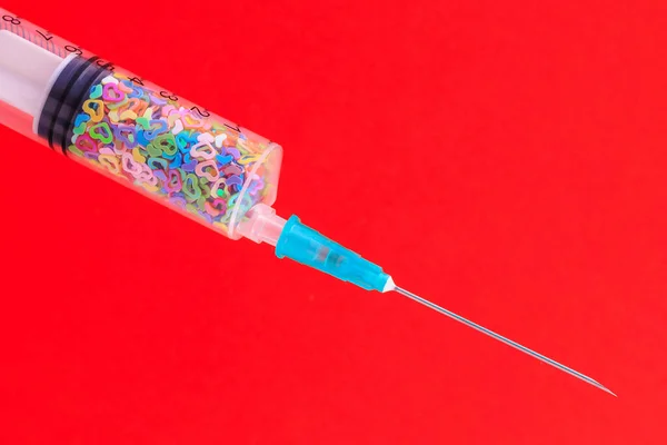 A classic disposable syringe filled with symbolic hearts. Love concept. Background with copy space for text. Red backdrop.