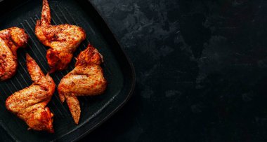 Raw chicken wings marinated in paprika and curry. Copy space. Raw meat on a grill pan. Dark background, top view.