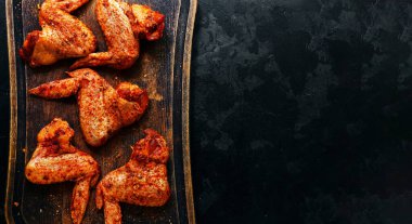 Raw chicken wings marinated in paprika and curry. Copy space. Raw meat on a cutting board. Dark background, top view.