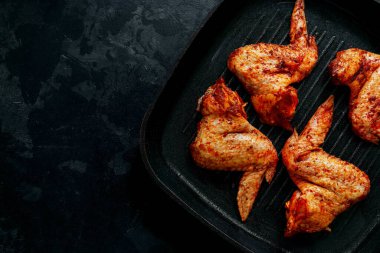 Raw chicken wings marinated in paprika and curry. Copy space. Raw meat on a grill pan. Dark background, top view.