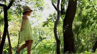 A child in a yellow dress walks in the park. The little girl walks in the forest on a sunny day.