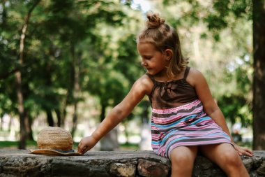Açık havada hasır şapkalı bir kız. 5 yaşında tatlı bir kızın portresi. Çocuk parkta oturuyordur. Boşluğu kopyala.