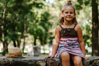 Açık havada hasır şapkalı bir kız. 5 yaşında tatlı bir kızın portresi. Çocuk parkta oturuyordur. Boşluğu kopyala.