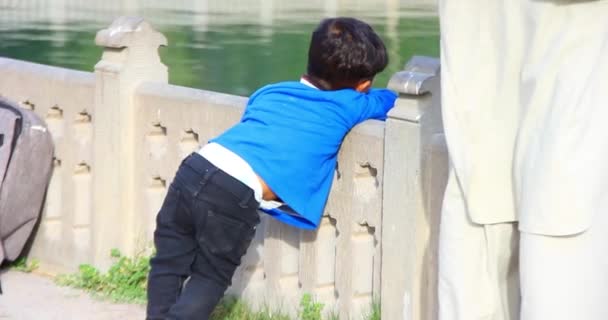 one kid wear a pant and a jacket in the winter season and looking at the lakeside face not showing, near stand his father, selective focus on the kid