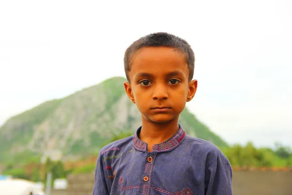 one poor Pakistani kid wears a shalwar kameez and looks at the camera, rainy day weather, selective focus on the kidone poor Pakistani kid wears a shalwar kameez and looks at the camera, rainy day weather, selective focus on the kid
