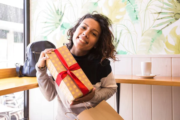 Young latin girl receiving a gift inside a coffee shop.